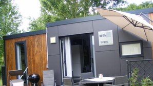 Ein moderner Außenbereich mit Terrasse, Tisch, Stühlen, Grill und Liegestuhl.