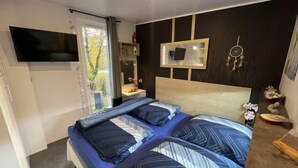 Ein Schlafzimmer mit Bett, Wandfernseher, Nachttisch und einem Fenster mit Vorhängen.