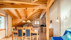 Un loft spacieux avec de hauts plafonds, des poutres apparentes, un coin repas avec des chaises, une cuisine et un canapé bleu.