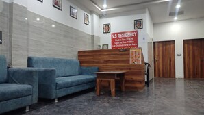 A reception area with a blue sofa, a wooden desk, and a sign indicating check-in and check-out times. - VS Residency (Mathura)