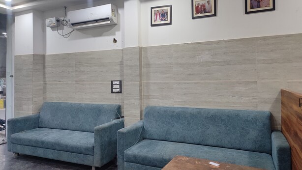 A waiting area with two blue sofas, an air conditioning unit, and framed pictures on the wall. - VS Residency (Mathura)
