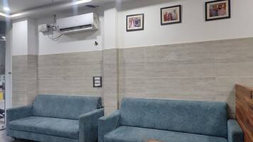 A waiting area with two blue sofas, an air conditioning unit, and framed pictures on the wall.