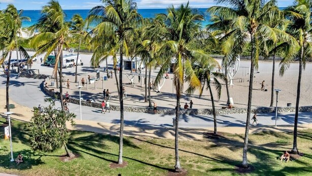 Une zone située au bord de la plage, agrémentée de palmiers, d’une promenade dallée et offrant une vue sur l’océan.
