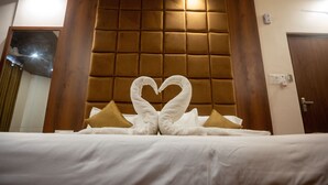 A hotel room with a large bed, a tufted headboard, and a heart-shaped towel decoration. - Kiran Palace Varanasi (Varanasi)