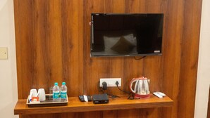 A wooden reception desk with a flat-screen TV mounted above it, a power outlet, a coffee maker, a tray with a bottle of Bisleri water, a cup, and a remote control. - Kiran Palace Varanasi (Varanasi)