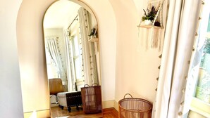 A room with a wooden floor, a grey upholstered sofa, a mirror, and a wicker basket.