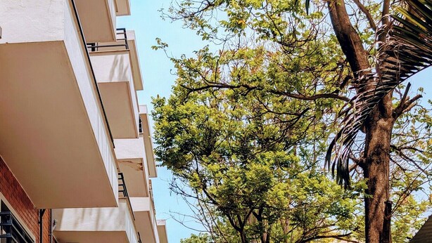 Um edifício com várias andares, varandas, um caminho pavimentado e vegetação exuberante.