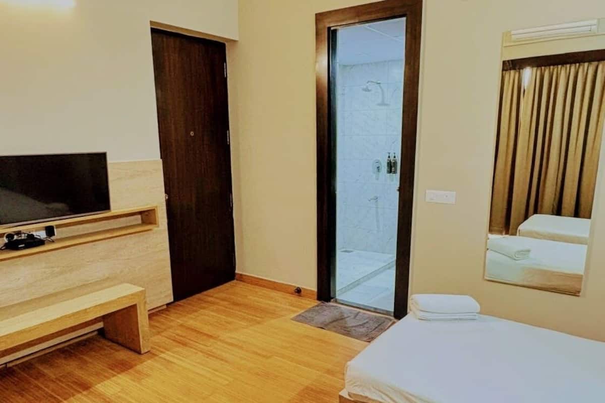 A hotel room with a bed, a TV, a wooden bench, a door, and a shower area.
