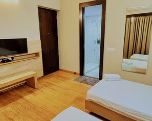 Ein Hotelzimmer mit einem Bett, einem Fernseher, einer hölzernen Bank, einer Tür und einer Duschkabine.