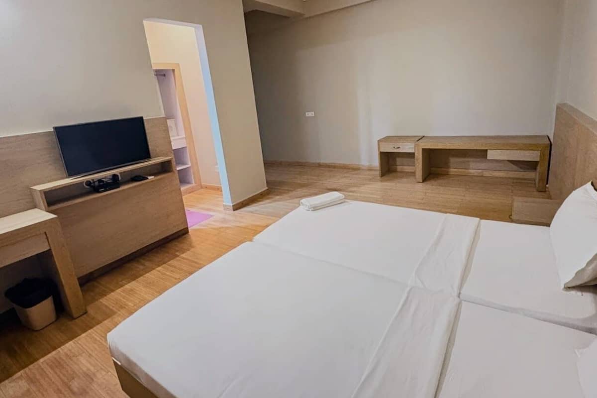 A hotel room with a bed, a TV, a desk, and a bench.
