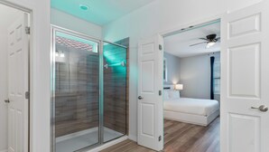 A modern bedroom with a glass shower, a bed, and a ceiling fan. - Arcade, Futuristic Theater, Triple 86” TV Wall, EV Charger, Waterpark - Epic Oasis (Davenport)