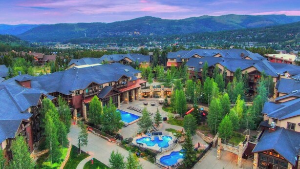 Un resort con varias edificaciones, un área de piscina central y vegetación circundante.
