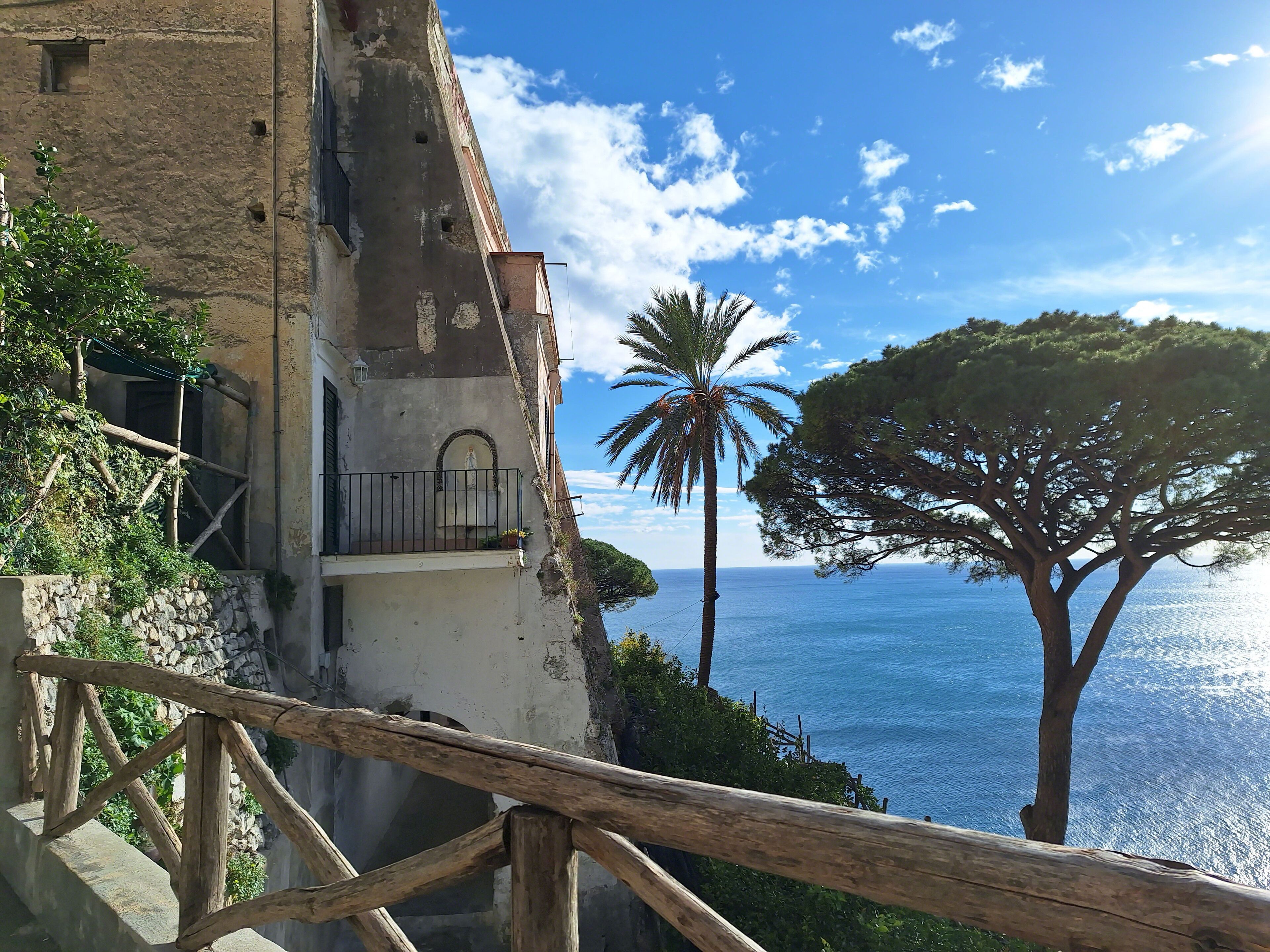 Un bâtiment situé sur la côte, doté d’un balcon donnant sur la mer, d’un palmier et d’une rambarde en bois.