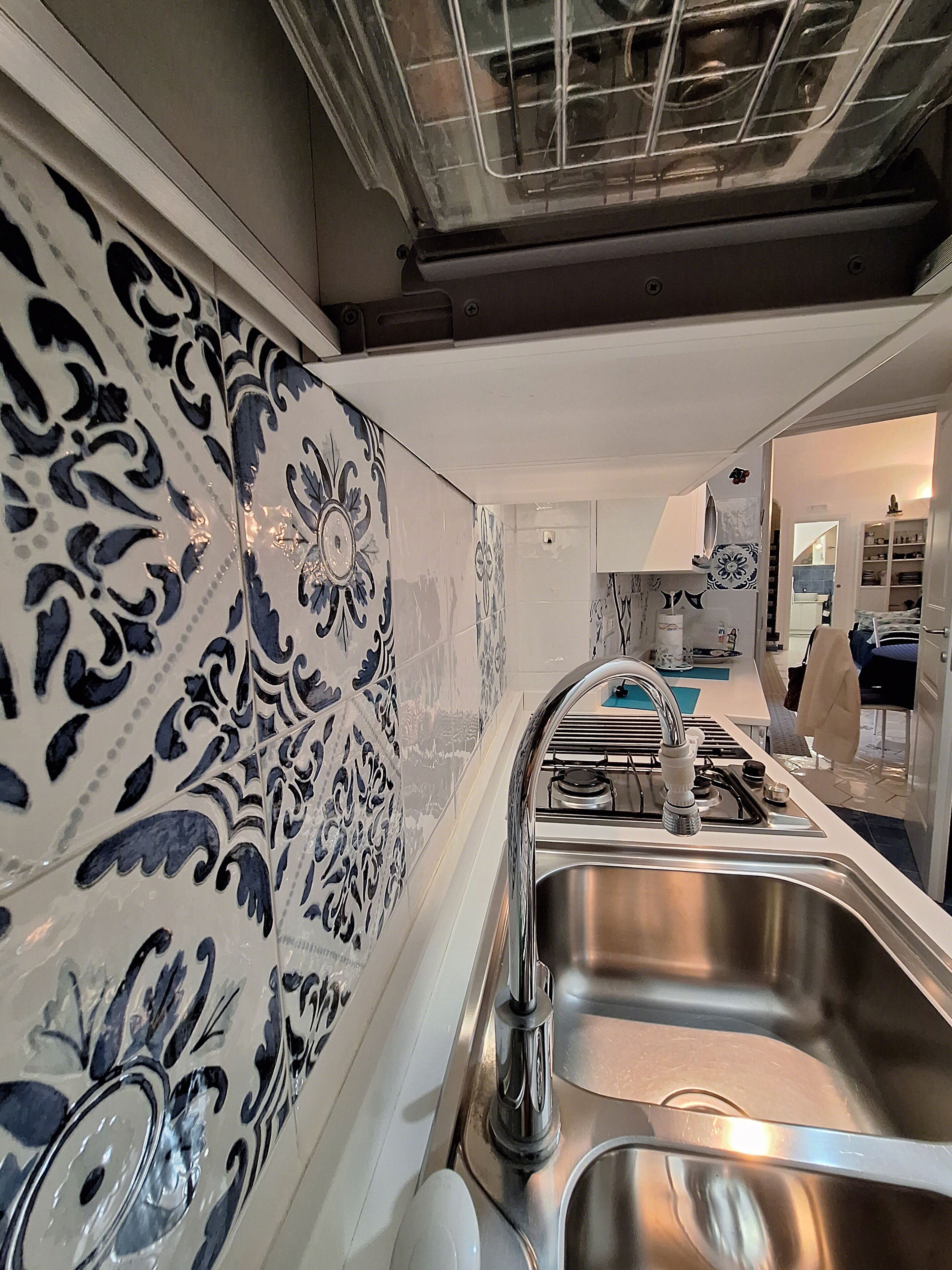 Une cuisine dotée d’un évier en acier inoxydable, de meubles blancs et de carreaux aux motifs bleus et blancs.