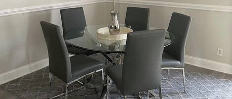 A dining area with a round glass table, black chairs, a chandelier, and a mirror on the wall.