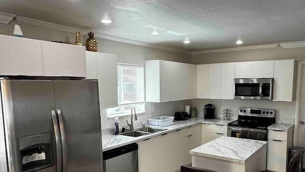 A modern kitchen with stainless steel appliances, a marble island, and bar stools.