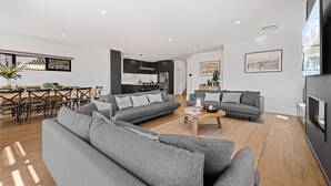 En moderne stue med grå sofaer, et træbord og et spiseområde med træstole og et bord.
