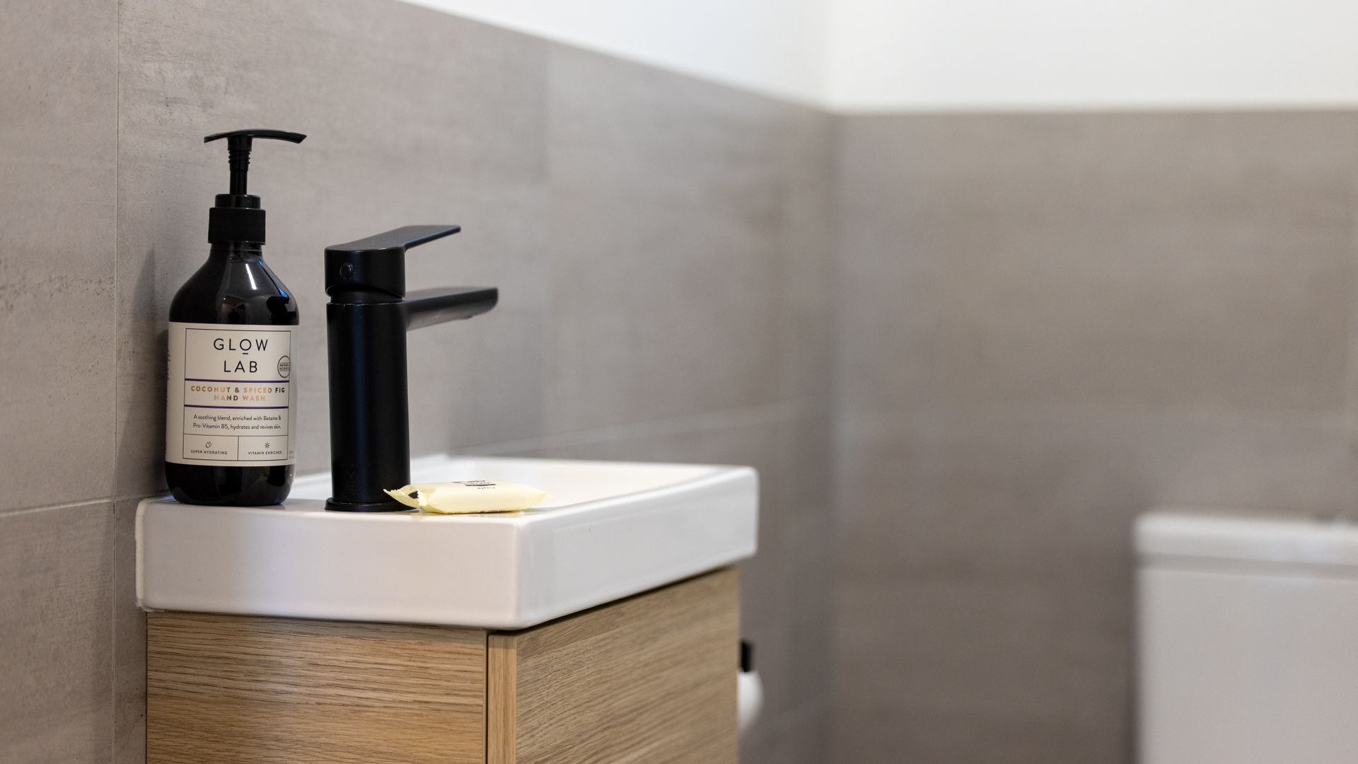 A bathroom sink with a bottle of Glow Lab Coconut & Spiced Fig hand wash and a pump dispenser.