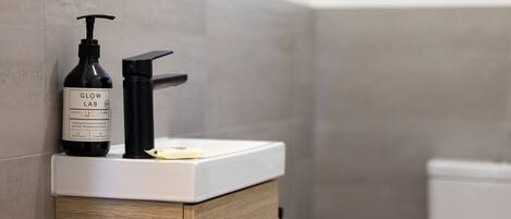 A bathroom sink with a bottle of Glow Lab Coconut & Spiced Fig hand wash and a pump dispenser.