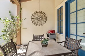 Een terras met een tafel, stoelen, een decoratieve wandhanger en een barbecue.