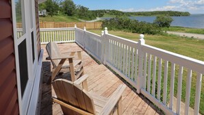 Una terraza de madera con dos sillas y un banco, con vistas a un lago y zona verde.