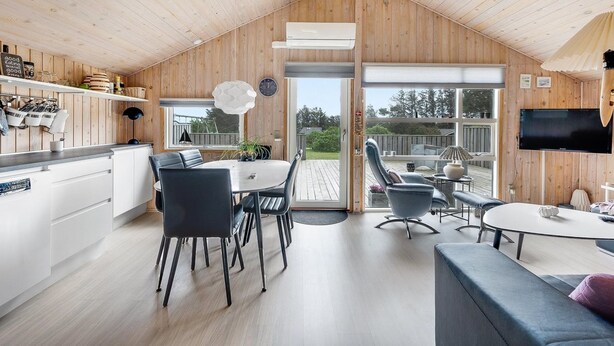 A modern kitchen with wooden walls, a dining area with a round table and chairs, and a large window overlooking a deck.