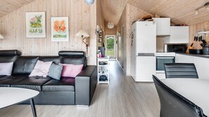 A modern interior with a black leather sofa, a dining table, and a kitchen area with a refrigerator and stove.
