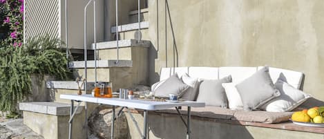 Une terrasse en pierre avec une table et des chaises en métal, un canapé blanc avec des coussins et une assiette de citrons.