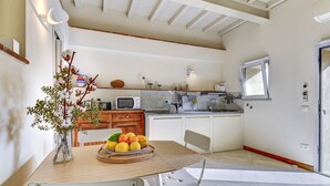 Una cocina con una mesa de comedor, sillas, un frutero y un florero con flores.