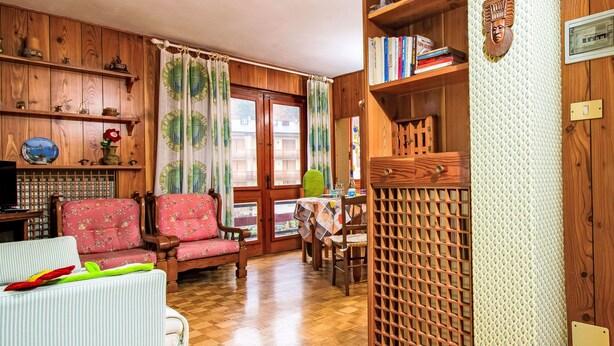 Una sala de estar acogedora con piso de madera, un sillón floral, un sofá blanco y una mesa de comedor con sillas.