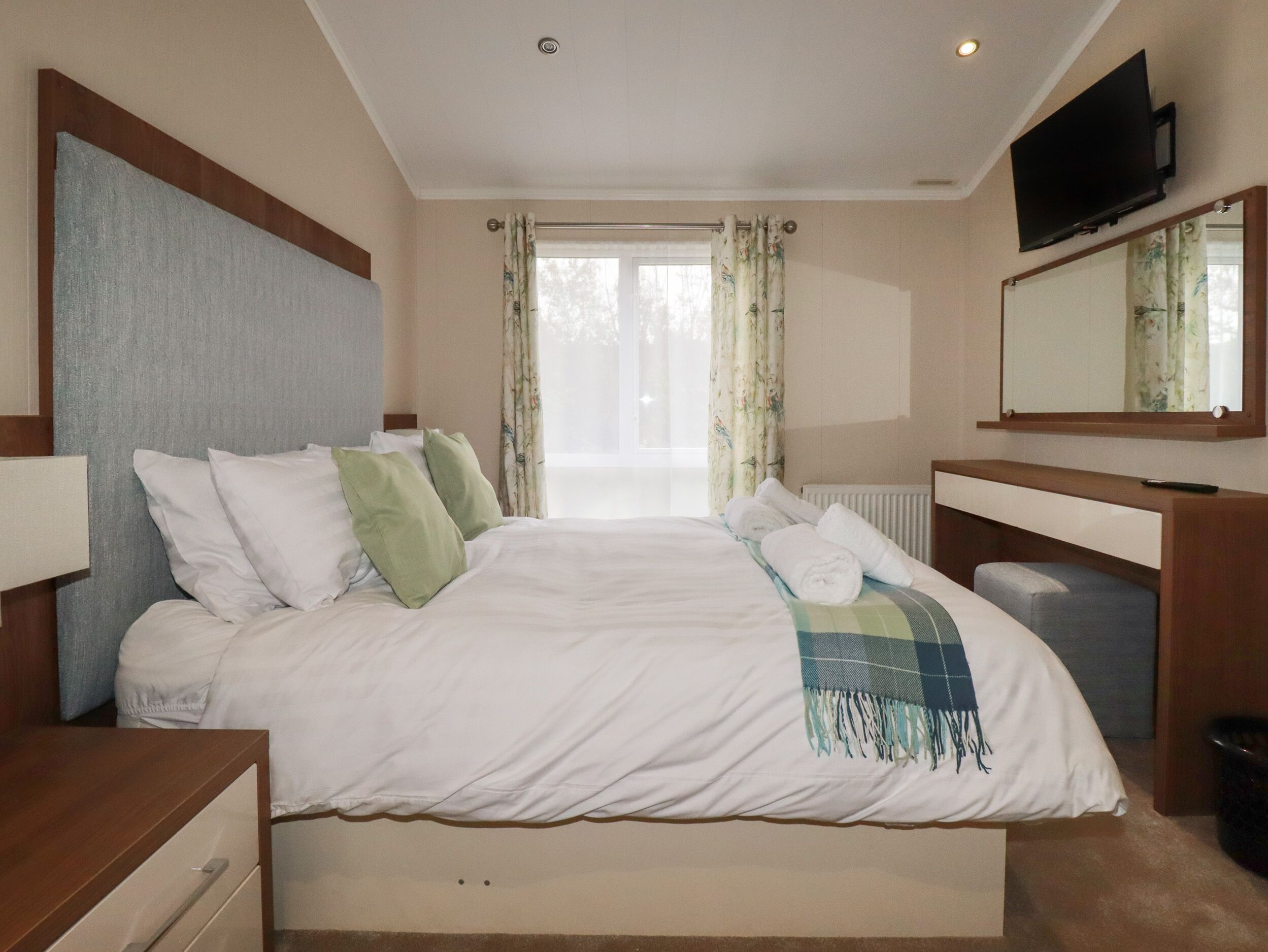Una camera d'albergo con un letto grande, un comodino, una TV a muro e una finestra con tende.