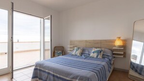 Een slaapkamer met een bed, een stoel, een bedlampje en een groot raam.