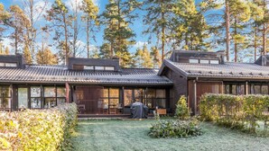 A traditional wooden house with a covered patio, surrounded by a grassy yard and tall trees.