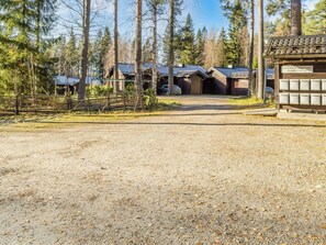 En grusbelagd parkeringsplats med ett trästaket, en rad byggnader med sluttande tak och en skylt som visar platsens läge.