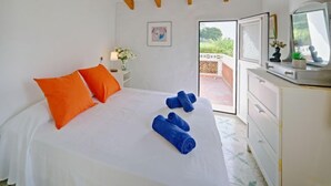 A bedroom with a bed, orange pillows, blue towels, a white dresser, a mirror, and a ceiling fan. - Casa Germaine by Interhome (Jávea)