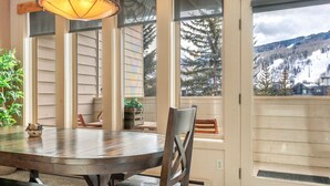 A dining area with a round table and chairs, large windows with a view of a snowy mountain, and a door with a view of the outside. - SunVail Condo - Steps from Bridge to Lionshead (Vail)