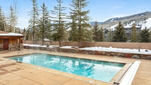 A pool area with a stone wall, a wooden cabin, and snow-covered ground. - SunVail Condo - Steps from Bridge to Lionshead (Vail)