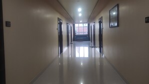Un largo pasillo bien iluminado con piso reflectante, que conduce a una habitación luminosa con un gran ventanal.