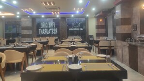 Un restaurante con varias mesas, sillas y una zona de cocina visible a través de paredes de vidrio.