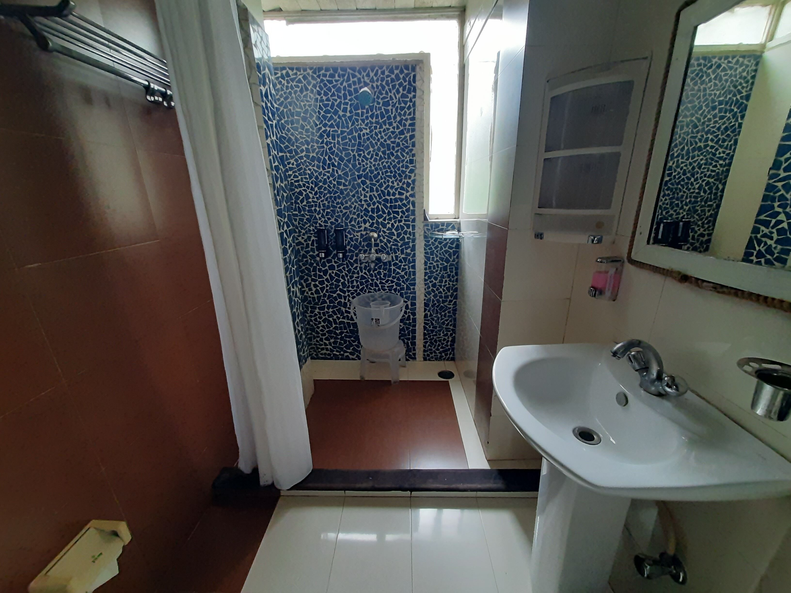 Une salle de bain avec un lavabo blanc, un miroir et un espace douche aux carreaux de mosaïque bleus.