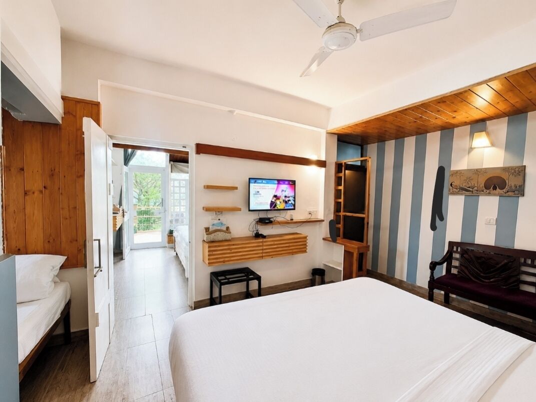 Habitación de hotel con cama, televisión, banca de madera y vista al exterior.