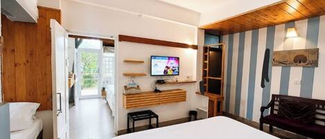 Habitación de hotel con cama, televisión, banca de madera y vista al exterior.