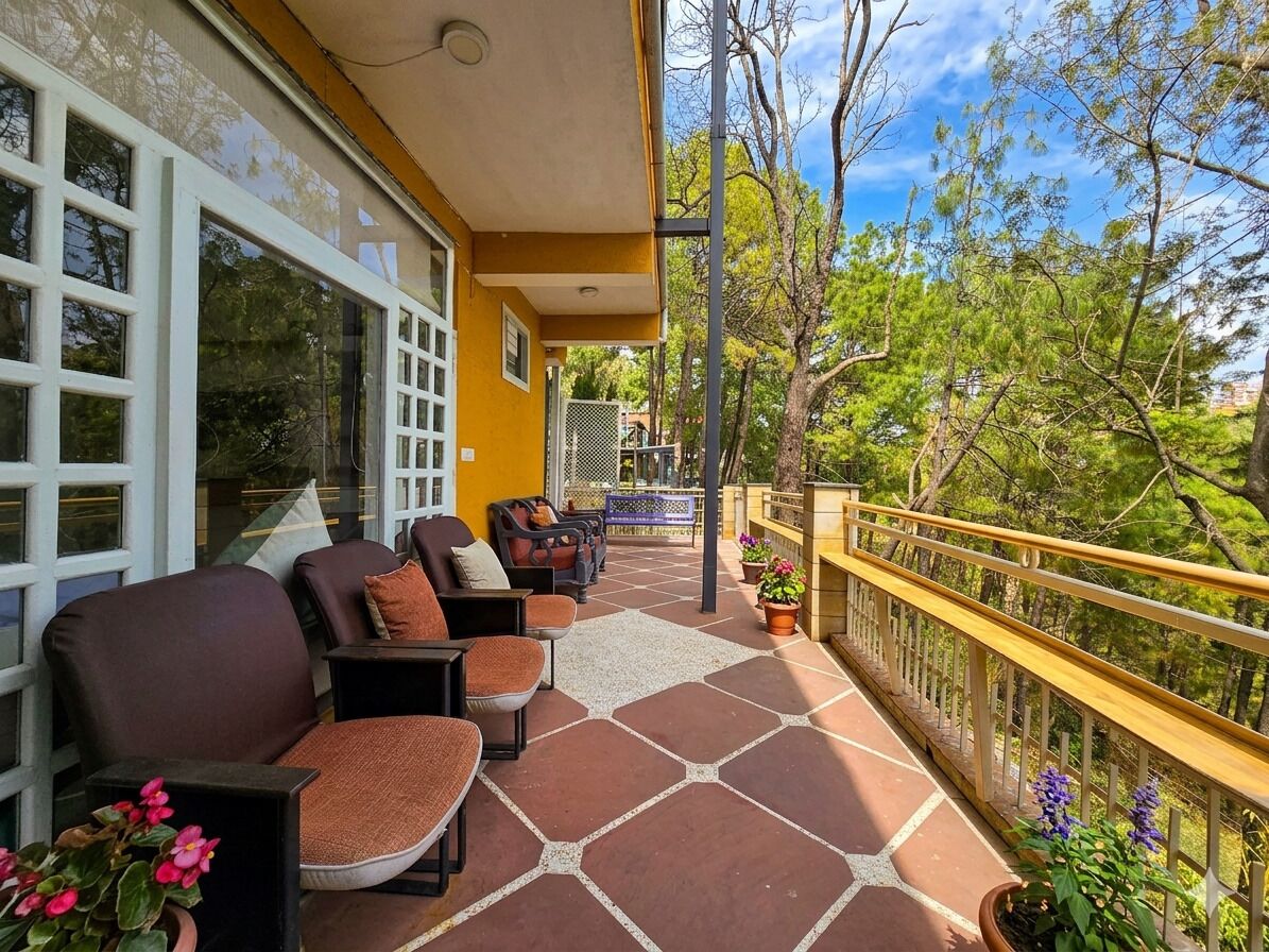 A balcony with outdoor seating, a yellow railing, and a view of trees and buildings.