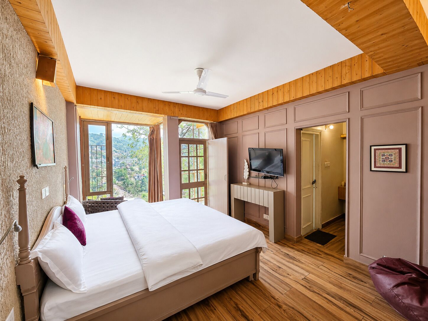 Un dormitorio con cama, televisión, ventilador de techo y vistas al exterior.