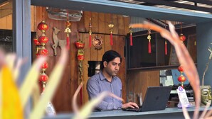 Un homme travaille à un bureau en bois, un ordinateur portable devant lui, et il est entouré de décorations traditionnelles aux couleurs rouge et or.
