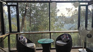Une véranda avec des fauteuils en osier, une table en verre et un ventilateur.