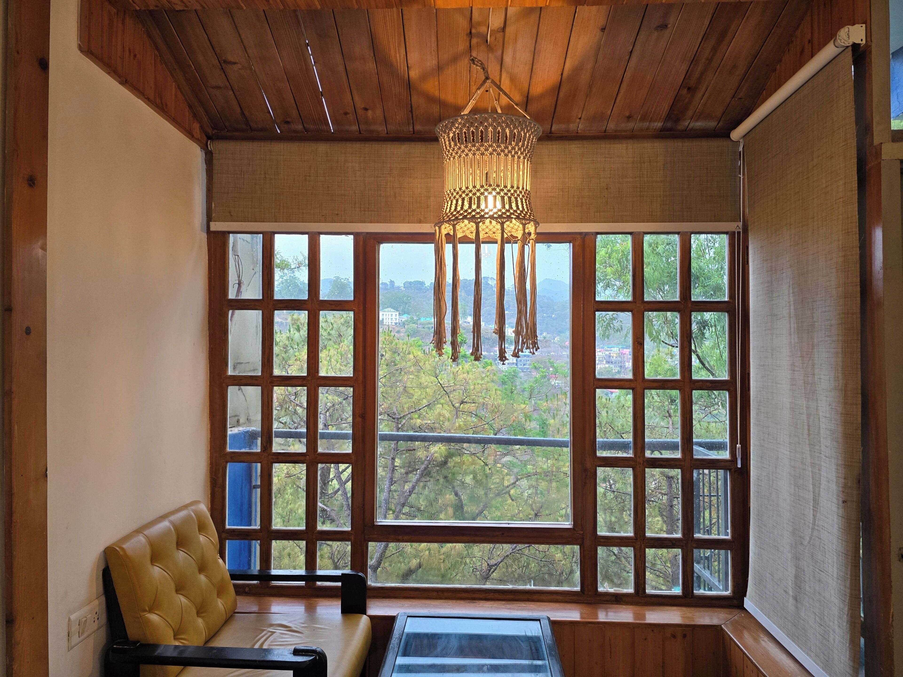 Una habitación con un ventanal grande, una lámpara colgante, un banco acolchado y techo de madera.