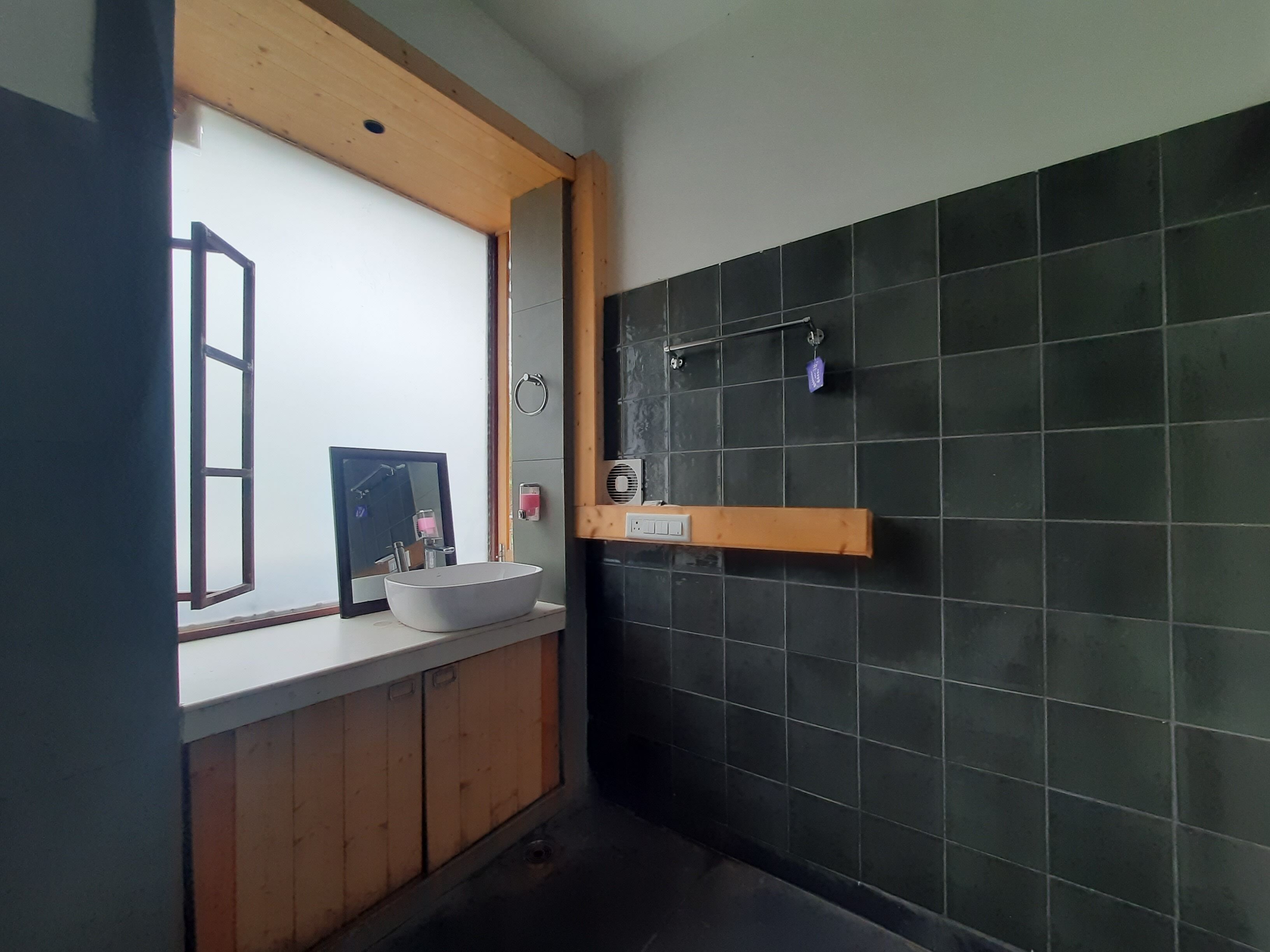 Un baño con tocador de madera, un espejo grande, lavabo sobre encimera y zona de ducha con azulejos negros.