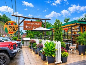A Sunrise Cottage Hotel & Cafe with a wooden sign, outdoor seating, and potted plants.
