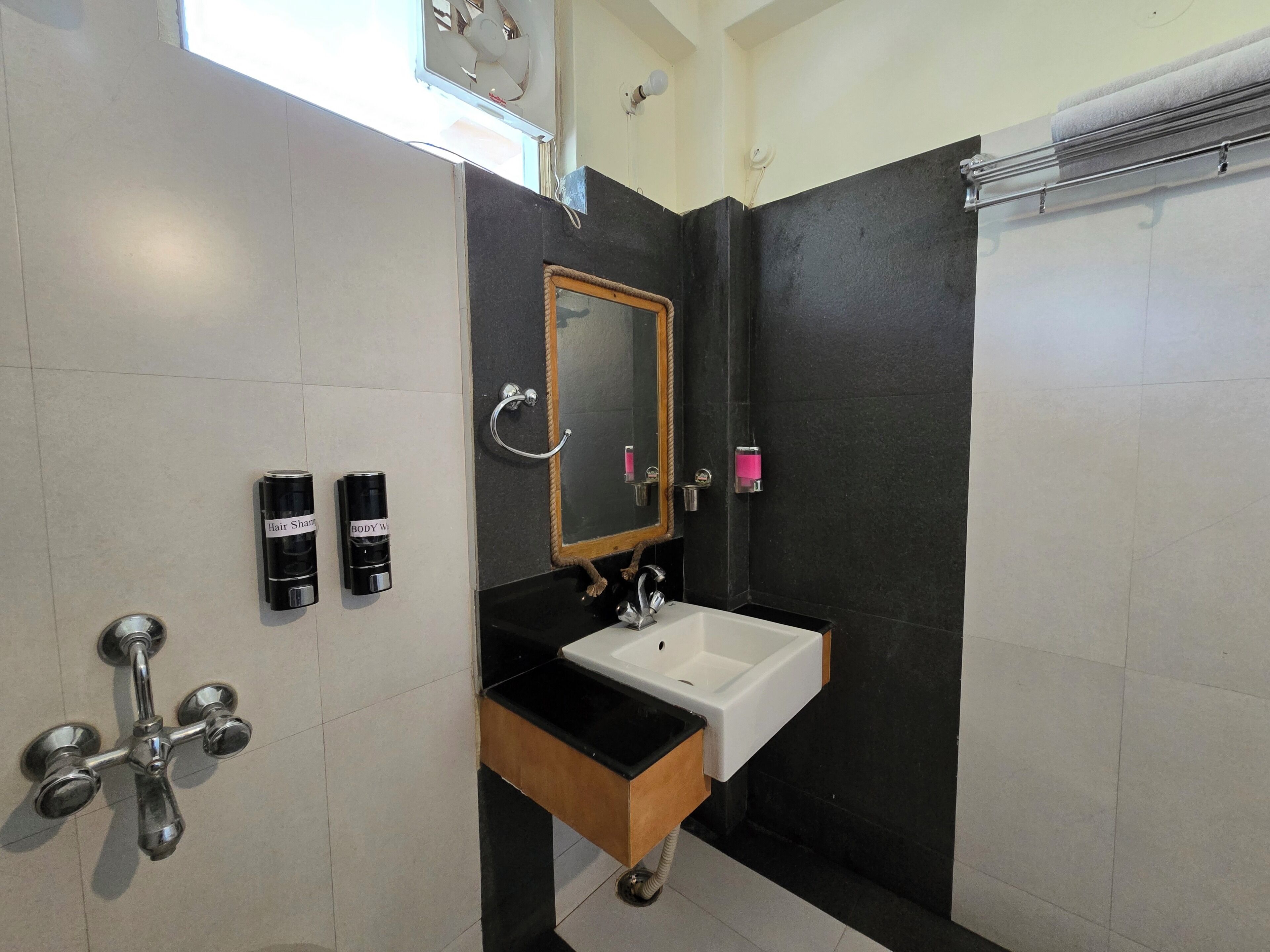 A bathroom with a white sink, black countertop, and a mirror with a wooden frame. There are two hair spray dispensers and a towel rack.
